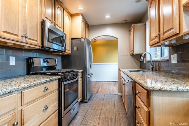 kitchen with stainless steel appliances, a sink, arched walkways, tasteful backsplash, and baseboards