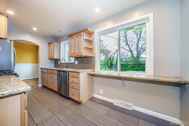 kitchen featuring appliances with stainless steel finishes, arched walkways, light brown cabinetry, open shelves, and baseboards