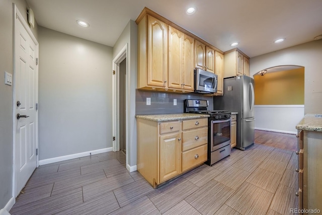 kitchen featuring stainless steel appliances, arched walkways, baseboards, light brown cabinetry, and recessed lighting