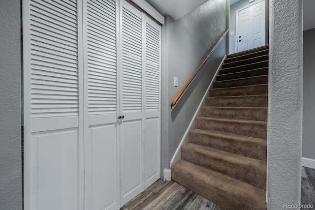 stairway with wood finished floors, a textured wall, and baseboards