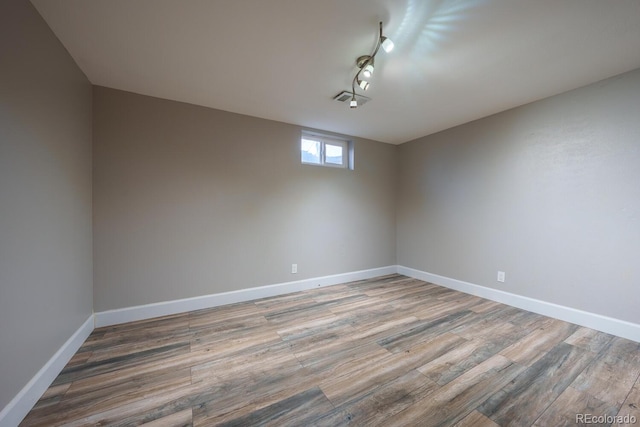 spare room with wood finished floors, baseboards, and rail lighting