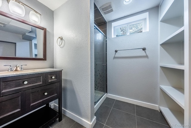 bathroom with a shower stall, vanity, baseboards, tile patterned floors, and a textured wall
