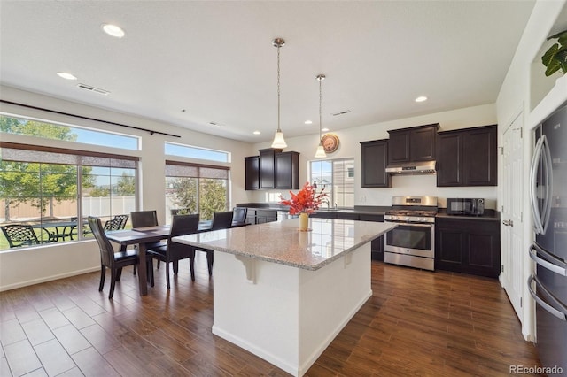 kitchen featuring under cabinet range hood, stainless steel appliances, dark wood-style flooring, and a center island