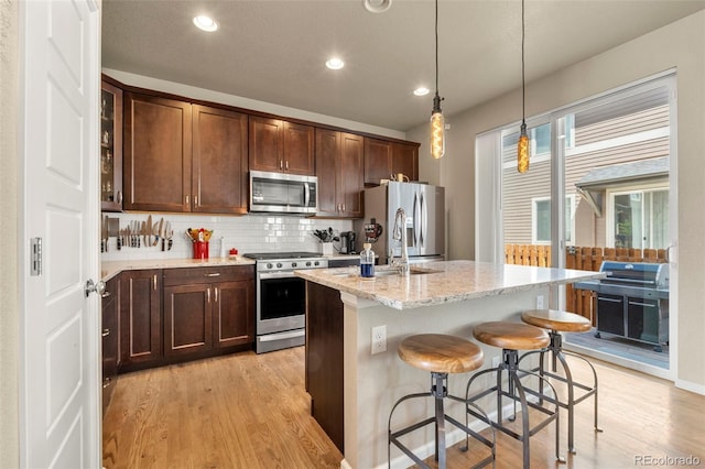 11235 S Neu Towne Cir, Parker, CO 80134 - kitchen with appliances with stainless steel finishes, light wood-type flooring, a kitchen island with sink, decorative backsplash, and light stone counters