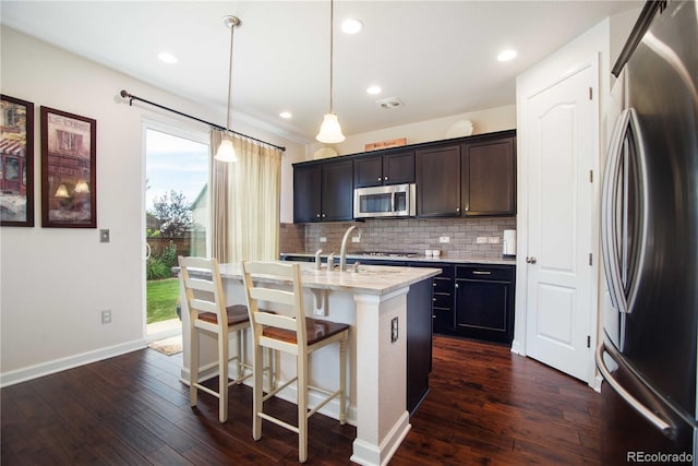 25536 E 1st Ave, Aurora, CO 80018 - kitchen featuring stainless steel appliances, tasteful backsplash, dark wood-style floors, an island with sink, and a breakfast bar area