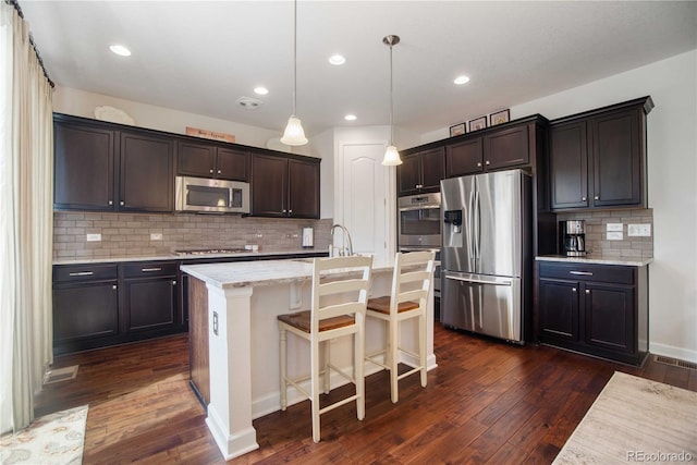 25536 E 1st Ave, Aurora, CO 80018 - kitchen featuring stainless steel appliances, dark wood-style floors, dark brown cabinetry, backsplash, and a kitchen island with sink