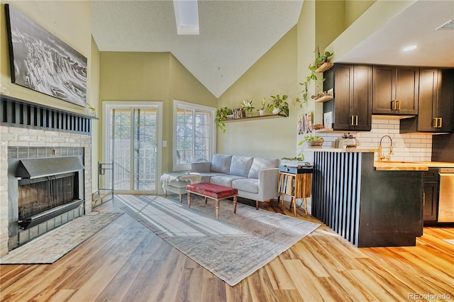 living room featuring a fireplace, high vaulted ceiling, sink, and light hardwood / wood-style floors