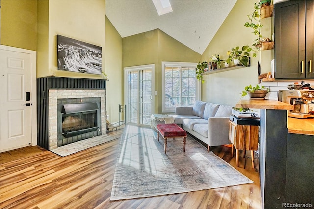 living room with a fireplace, high vaulted ceiling, a skylight, and light hardwood / wood-style flooring