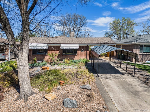 single story home with a detached carport, concrete driveway, a shingled roof, and brick siding
