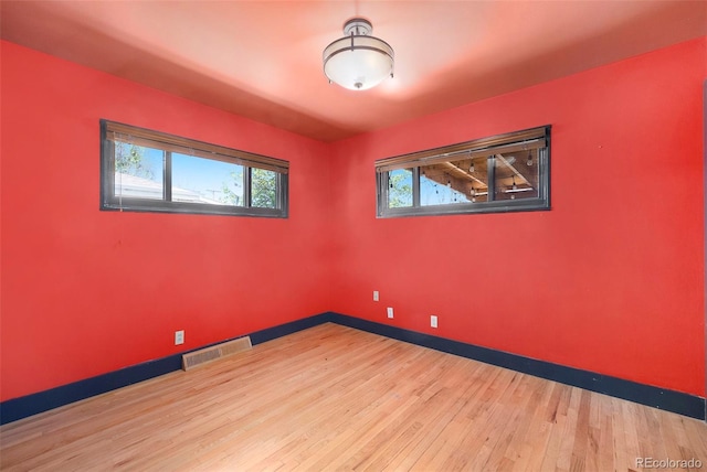 spare room with wood finished floors, visible vents, and baseboards