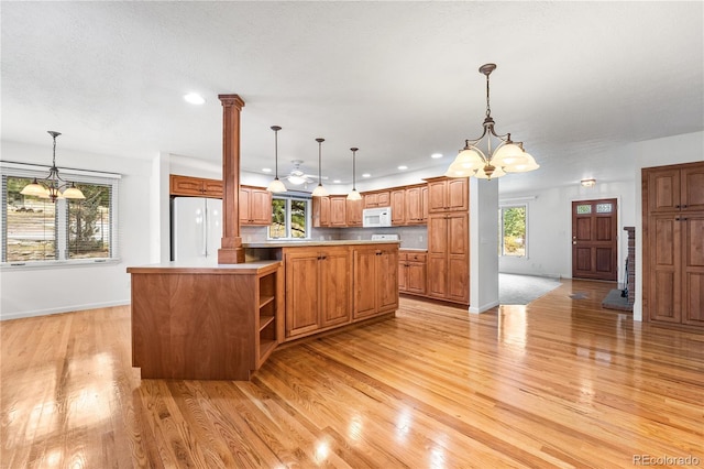 kitchen featuring light wood-type flooring, white appliances, decorative light fixtures, and a healthy amount of sunlight