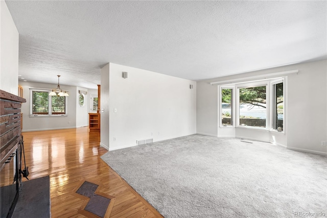 unfurnished living room with a textured ceiling, a brick fireplace, a chandelier, and light hardwood / wood-style floors