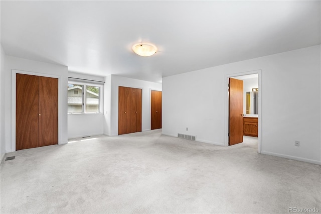 interior space featuring ensuite bath, light carpet, and two closets