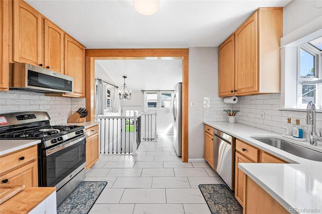 kitchen featuring appliances with stainless steel finishes, tasteful backsplash, a notable chandelier, decorative light fixtures, and sink