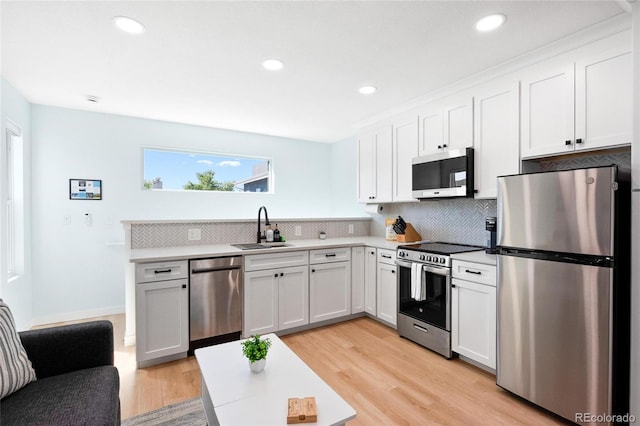 kitchen with white cabinets, stainless steel appliances, decorative backsplash, sink, and light wood-type flooring