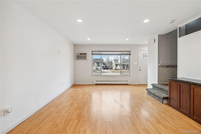 unfurnished living room with a baseboard radiator, a wall mounted air conditioner, and light hardwood / wood-style flooring