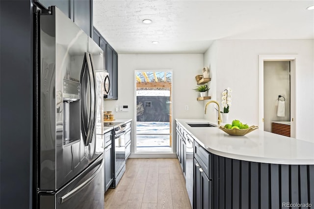 kitchen featuring sink, a textured ceiling, kitchen peninsula, stainless steel appliances, and light hardwood / wood-style floors