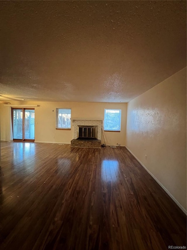 unfurnished living room featuring hardwood / wood-style floors, a textured ceiling, and a brick fireplace