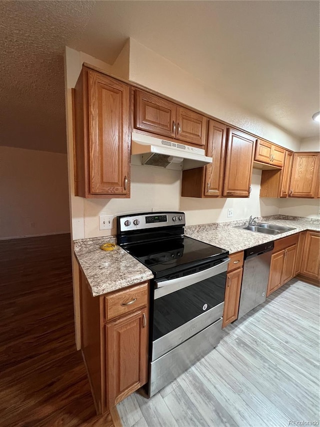 kitchen with appliances with stainless steel finishes, light hardwood / wood-style floors, light stone counters, and sink