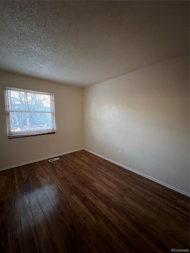 empty room with dark hardwood / wood-style flooring and a textured ceiling