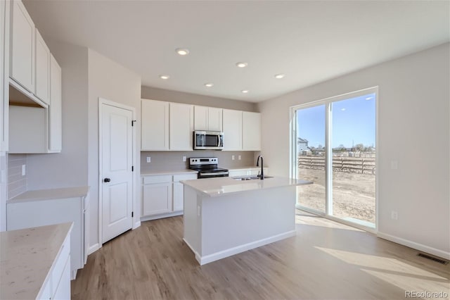 kitchen featuring white cabinets, sink, an island with sink, appliances with stainless steel finishes, and light hardwood / wood-style floors