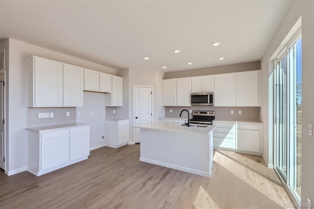 kitchen with stainless steel appliances, white cabinetry, light hardwood / wood-style floors, and an island with sink