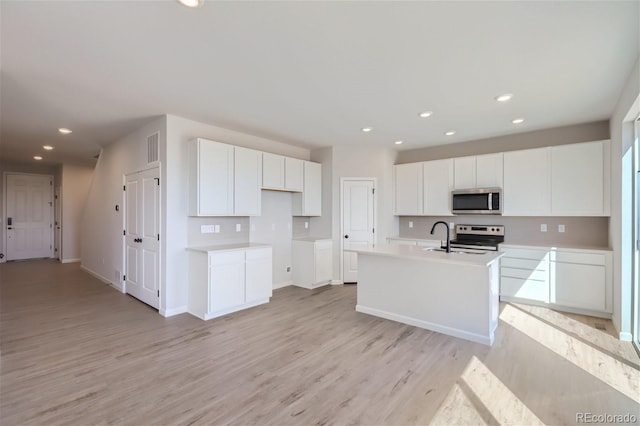 kitchen featuring sink, light hardwood / wood-style flooring, an island with sink, white cabinets, and appliances with stainless steel finishes