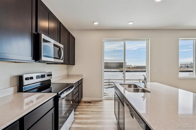 kitchen with stainless steel appliances, light wood finished floors, a sink, and light countertops