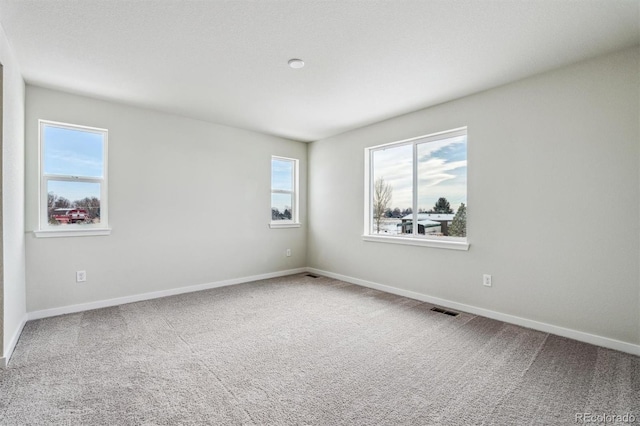 empty room featuring carpet, visible vents, and baseboards