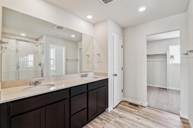 bathroom featuring a spacious closet, wood finished floors, a sink, and a shower stall