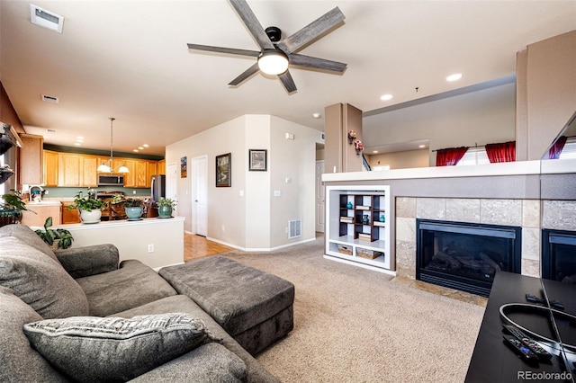 carpeted living room featuring a tiled fireplace and ceiling fan