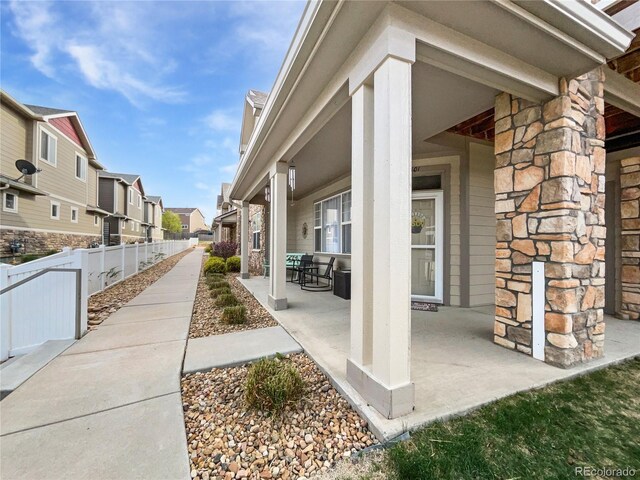 view of side of home with a patio, fence, a residential view, and stone siding