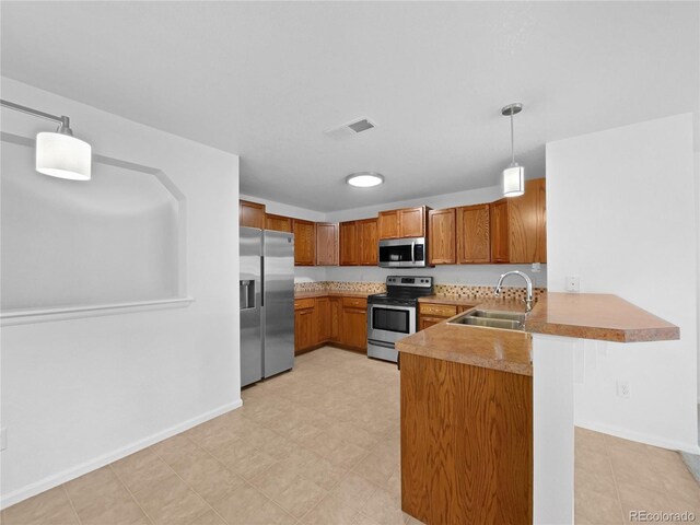 kitchen with brown cabinetry, decorative light fixtures, a sink, a peninsula, and stainless steel appliances