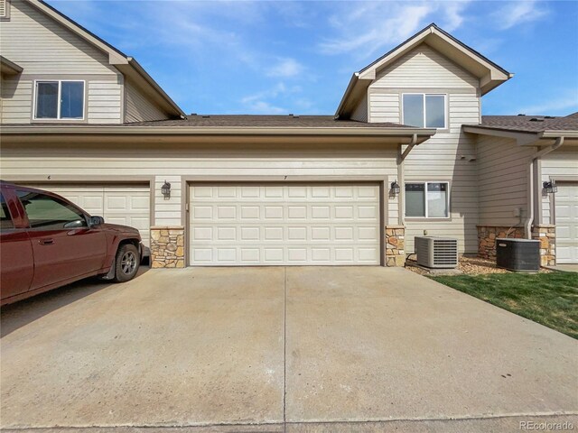 view of front of property with an attached garage, concrete driveway, cooling unit, and stone siding