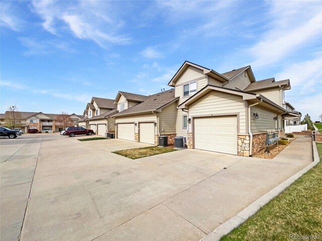 view of front facade featuring a residential view, stone siding, a garage, central AC unit, and driveway