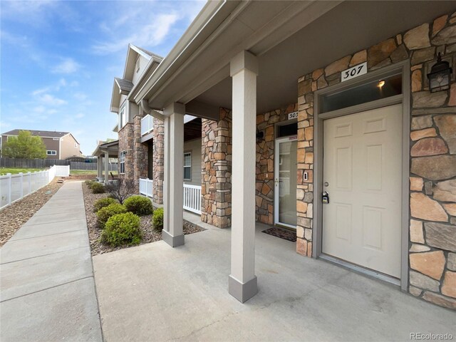 entrance to property featuring a porch, fence, and stone siding