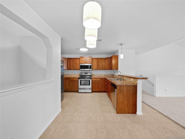 kitchen featuring baseboards, a peninsula, appliances with stainless steel finishes, and brown cabinets