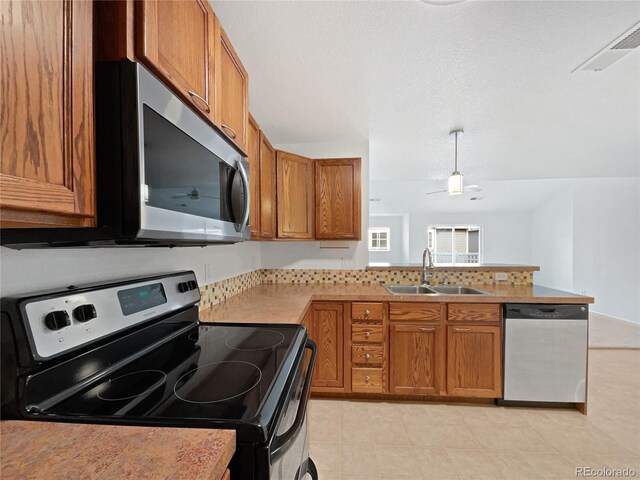 kitchen featuring brown cabinets, appliances with stainless steel finishes, a sink, light countertops, and a peninsula