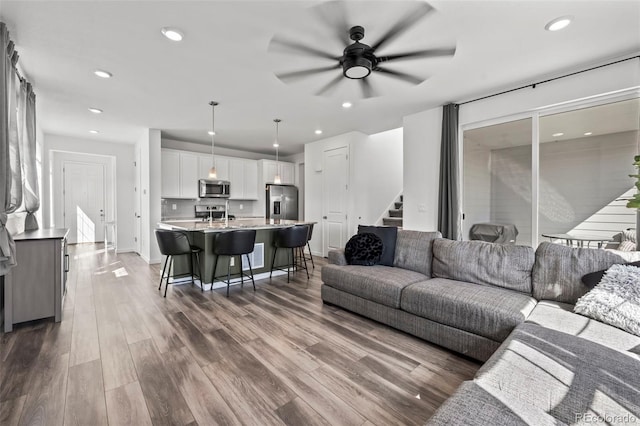 living area with wood finished floors, baseboards, recessed lighting, ceiling fan, and stairs