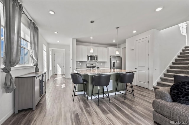 kitchen with light wood finished floors, open floor plan, a kitchen bar, white cabinets, and stainless steel appliances