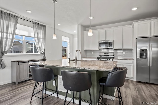 kitchen with a sink, tasteful backsplash, wood finished floors, appliances with stainless steel finishes, and light stone countertops