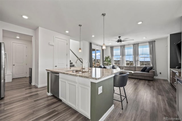 kitchen with a sink, open floor plan, appliances with stainless steel finishes, white cabinets, and dark wood-style flooring