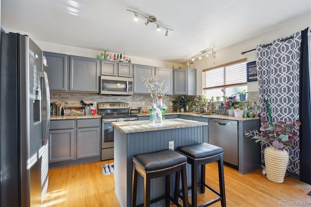 kitchen with a breakfast bar, decorative backsplash, light wood-type flooring, appliances with stainless steel finishes, and a kitchen island