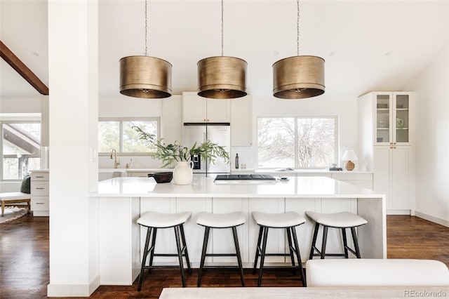 kitchen featuring stainless steel built in refrigerator, a kitchen breakfast bar, white cabinets, glass insert cabinets, and dark wood-style flooring