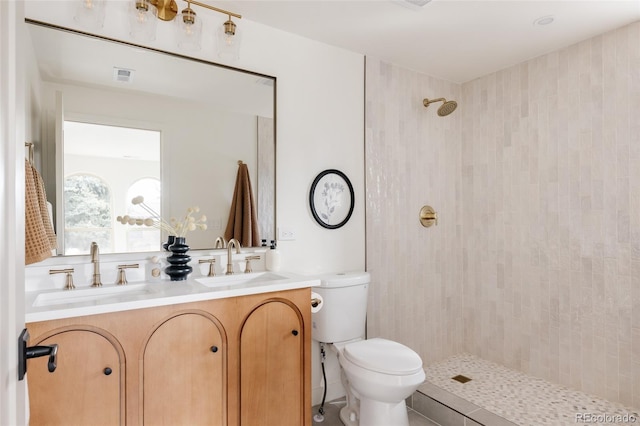 bathroom with visible vents, a sink, a tile shower, and toilet