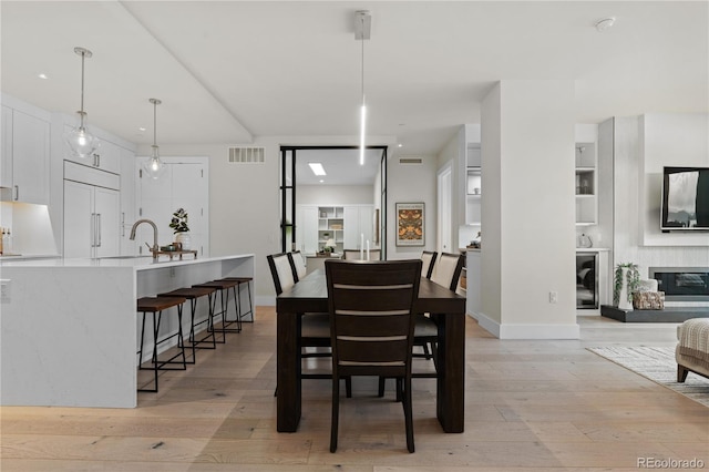 dining room featuring a glass covered fireplace, visible vents, light wood-style flooring, and baseboards