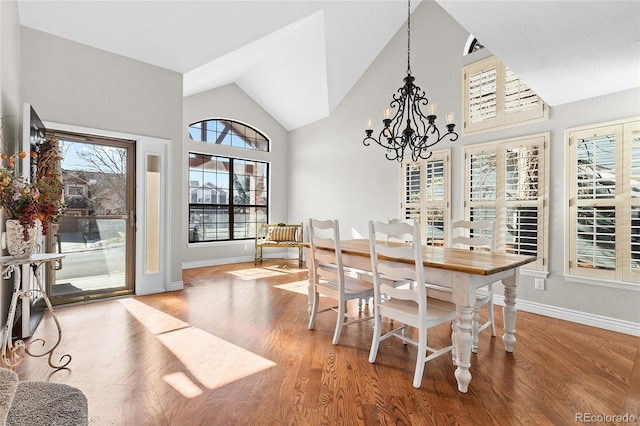 dining area featuring a chandelier, high vaulted ceiling, baseboards, and wood finished floors