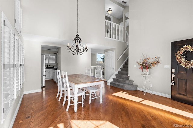 dining area with a towering ceiling, baseboards, stairway, and wood finished floors