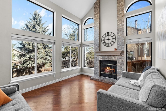 interior space featuring high vaulted ceiling, a fireplace, wood finished floors, and baseboards