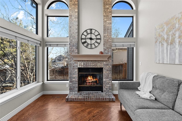 sitting room featuring a fireplace, wood finished floors, a towering ceiling, and baseboards